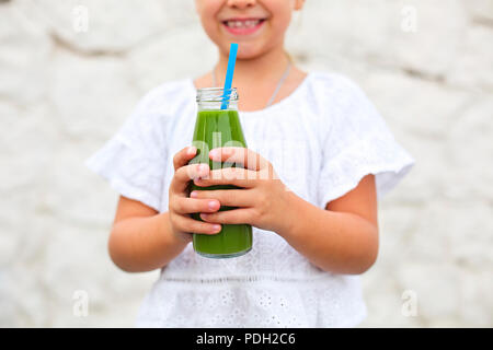 Petite fille c'est boire du jus vert frais utilisant la paille à l'extérieur. Close up Banque D'Images