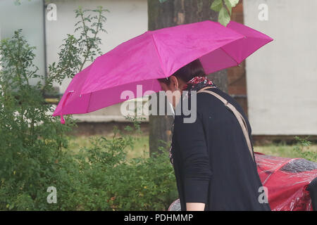 Londres. UK 10 Aug 2018 - une femme protège sous un parapluie de couleur rose comme il commence à pleuvoir dans entre éclaircies à Londres. D'après le Met Office le temps incertain est susceptible de se poursuivre au cours des prochains jours. Credit : Dinendra Haria/Alamy Live News Banque D'Images