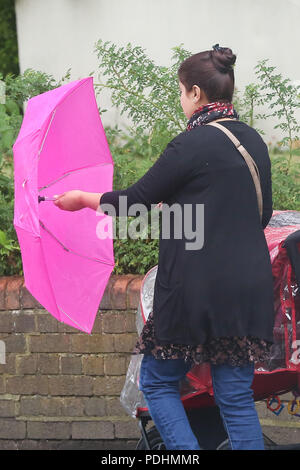 Londres. UK 10 Aug 2018 - une femme protège sous un parapluie de couleur rose comme il commence à pleuvoir dans entre éclaircies à Londres. D'après le Met Office le temps incertain est susceptible de se poursuivre au cours des prochains jours. Credit : Dinendra Haria/Alamy Live News Banque D'Images