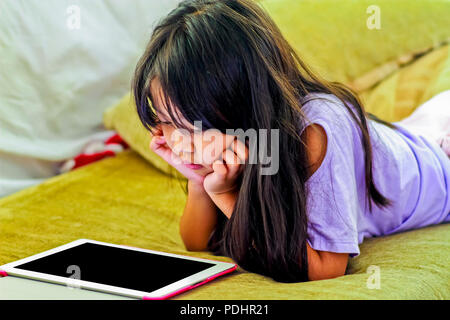 Cute young girl couchée sur le canapé à la recherche d'écran de tablette numérique Banque D'Images