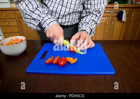 Man slicing tomatoes avec un beau bleu sur une planche à découper dans une cuisine maison Banque D'Images