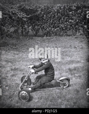 Années 1960, historiques, jeune garçon assis sur un trois-roues métal pédales toy-kart en dehors de l'herbe dans un jardin, England, UK. Banque D'Images