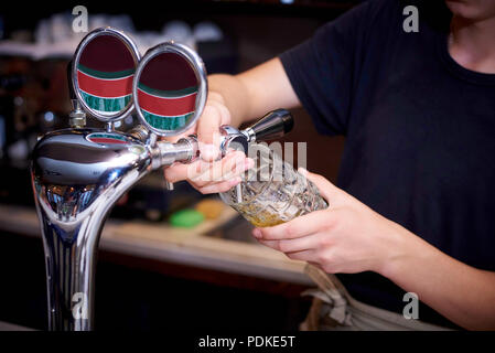 Le barman verse de la bière dans la tasse de l'eau du robinet. Banque D'Images