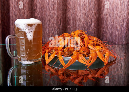 La langouste bouillie et tasse avec de la bière froide sur une table en verre avec la réflexion. Banque D'Images