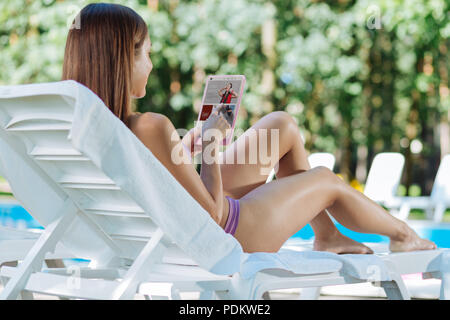 Femme moderne la regarder de vieilles photos sur l'ordinateur portable tout en étant allongé près de la piscine Banque D'Images