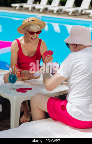 Femme portant des lunettes rouge à la retraite jouent aux cartes avec mari Banque D'Images