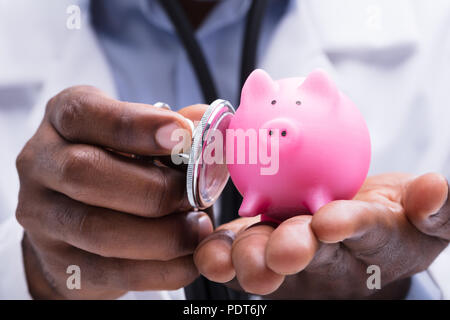 Close-up of a doctor Pink Piggybank miniature dans sa main avec stéthoscope Banque D'Images
