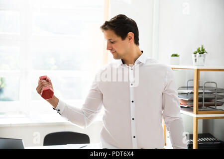 Jeune homme d'entraînement avec haltères courtes rouge in office Banque D'Images