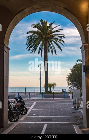 Vue sur un palmier le long de la côte méditerranéenne sur la Promenade des Anglais au moyen d'une porte voûtée de la Vieille Ville Vieille Ville de Nice, sur la côte Banque D'Images