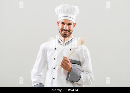 Portrait of smiling chef holding cuillère en bois sur fond gris. Banque D'Images