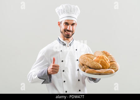 Baker holding bunch of pain et showing thumb up sur fond gris. Banque D'Images