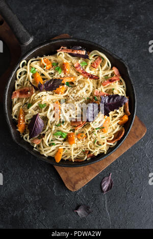 L'automne des pâtes avec du bacon et de citrouille dans poêle en fonte. Spaghetti maison pâtes potiron avec bacon, fromage parmesan et basilic sur noir, copiez l'espace. Aut Banque D'Images