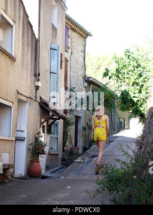 Une ambiance gaie et joliment habillés 16 ans fille aux cheveux blonds en se promenant dans les rues du vieux village de Cessenon marche loin de l'appareil photo Banque D'Images