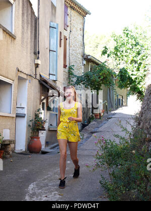 Une ambiance gaie et joliment habillés 16 ans fille aux cheveux blonds descendant une colline à travers les rues du vieux village de Cessenon, vers l'appareil photo Banque D'Images