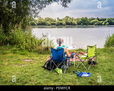 Jeune fille ou femme est assise à une table de pique-nique avec vue sur le lac à Mheuu Bridge Country Park dans le Gloucestershire. Banque D'Images