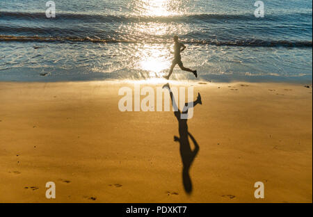 Seaton Carew, County Durham, Angleterre. United Kingdom. 11 août, 2018. Météo France : Après les orages de vendredi, le soleil se lève dans un ciel clair comme un jogger hits la plage sur un froid samedi matin à Seaton Carew sur la côte du comté de Durham. Credit : ALAN DAWSON/Alamy Live News Banque D'Images