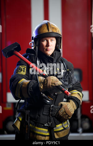 Photo de pompier avec marteau dans les mains près du feu Banque D'Images