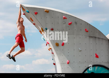 Photo de l'homme sport formés en short rouge accroché au mur d'escalade contre le ciel bleu avec des nuages Banque D'Images