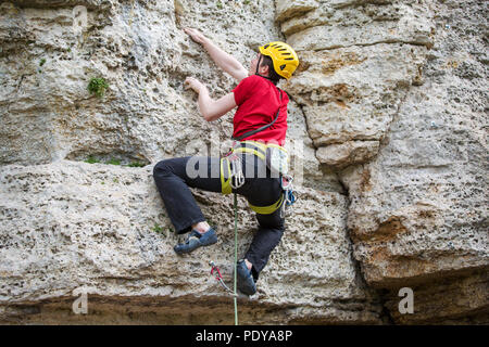 Photo de l'arrière du sports escalade homme à casque jaune sur la roche Banque D'Images