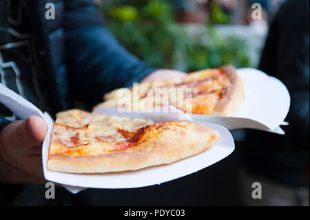 Deux gros morceaux de pizza dans les mains d'un homme. Le déjeuner dans la rue. L'alimentation de rue dans la ville de l'Europe. Espace libre pour le texte. Banque D'Images