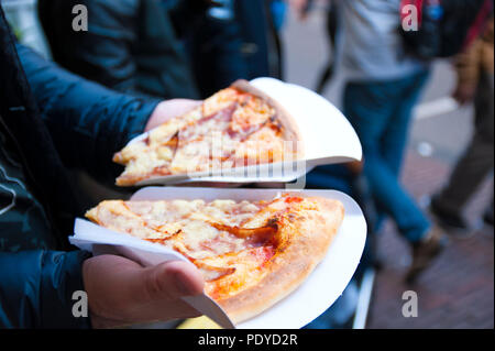 Deux gros morceaux de pizza dans les mains d'un homme. Le déjeuner dans la rue. L'alimentation de rue dans la ville de l'Europe. Espace libre pour le texte. Banque D'Images