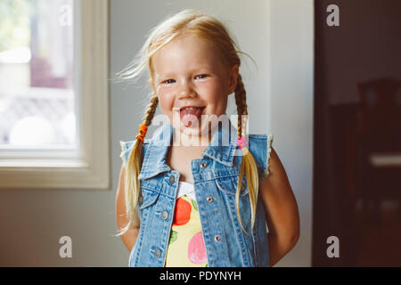 Closeup portrait of cute adorable blonde drôle white Caucasian preschool girl à la caméra en montrant la langue. La fille aux cheveux de lumière avec p Banque D'Images