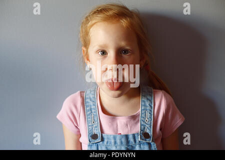 Closeup portrait of cute adorable drôle de roux blanc Caucasian preschool girl à la caméra en montrant la langue. Sourire de l'enfant de s'amuser. Banque D'Images