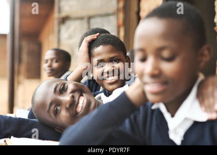 Les jeunes écoliers ougandais habillés dans un uniforme scolaire s'asseoir à l'extérieur sur des bancs en bois qui étudient pour leurs examens en classe avec de la brique en arrière-plan Banque D'Images