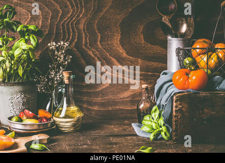 Les tomates de la ferme colorée sur table de cuisine rustique en bois sombre avec des ingrédients et des outils de cuisine. Arrière-plan de l'alimentation, style de vie encore, vue de face. Banque D'Images