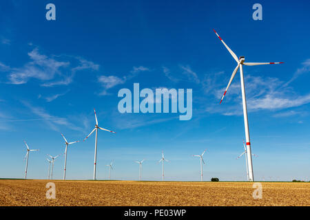 Beau paysage avec des terres agricoles jaune éoliennes blanc avec rayures rouges la production d'électricité sur le bleu de l'peu de ciel nuageux. Banque D'Images