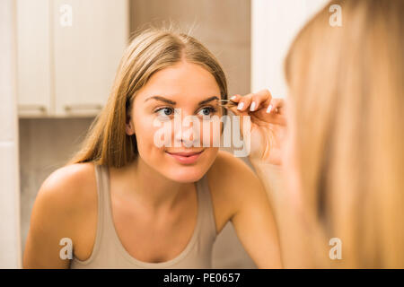 Belle femme l'Épilation sourcils dans une salle de bains privative. Banque D'Images