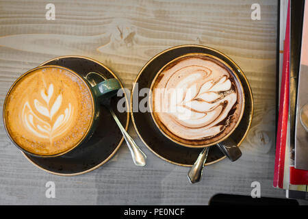 Pour elle et pour lui. Deux tasses sur la table. Une tasse de café, une autre tasse avec du chocolat chaud. Chaque verre est décoré avec un motif de lait. Une grande op Banque D'Images