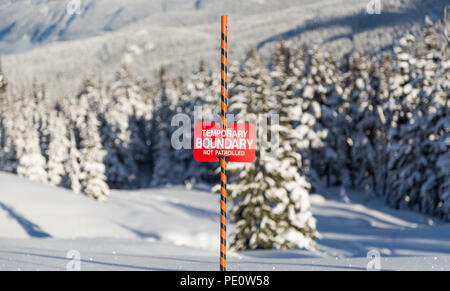 Traces dans la neige à côté d'un signe des limites de la zone de ski. Banque D'Images