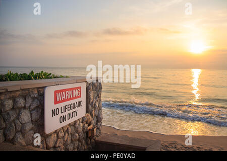 Panneau d'avertissement "pas de sauveteur en service' sur mur de pierre à la plage avec la mer et le ciel en arrière-plan le lever et copy space Banque D'Images