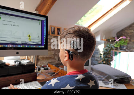 Vue arrière de garçon enfant avec technologie numérique implants cochléaires regarder l'écran jouer un jeu d'ordinateur à la maison au Royaume-Uni KATHY DEWITT Banque D'Images