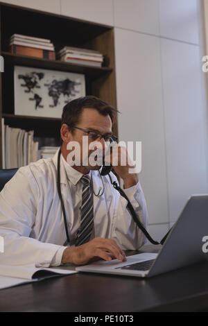 Doctor talking on landline while using laptop Banque D'Images
