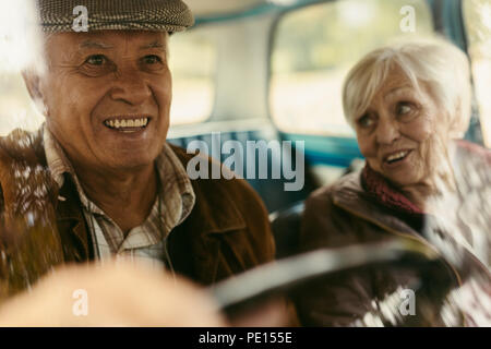 Smiling senior homme conduisant une voiture avec une femme sur le siège passager. Vieux couple heureux pour rouler en voiture. Banque D'Images