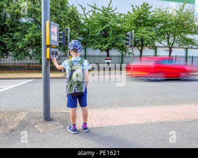 La vue jour petit enfant garçon avec sac à dos en appuyant sur le bouton signal pour piétons pour traverser la route britannique. Banque D'Images