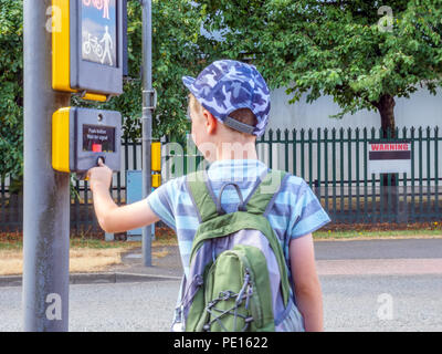 La vue jour petit enfant garçon avec sac à dos en appuyant sur le bouton signal pour piétons pour traverser la route britannique. Banque D'Images