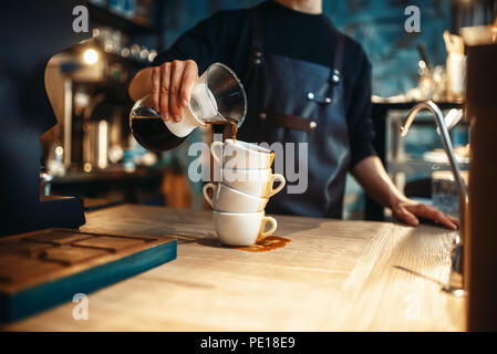 Barista mâle verse du café noir sur une pile de tasses, café comptoir et machine à expresso sur l'arrière-plan. Barman travaille dans une cafétéria, barman de l'occupation Banque D'Images