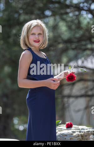 Jolie jeune femme blonde preteenn, fashion shoot. Comité permanent par rock, avec une rose rouge dans la main. 3/4 profil, robe bleue, modèle publié. Banque D'Images