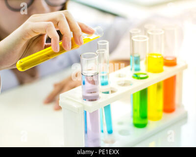 La main libre de female scientist holding test tube contiennent un liquide jaune versant à l'autre in laboratory Banque D'Images