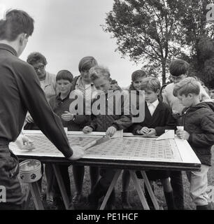 Années 1960, à l'extérieur à une fête du village, les jeunes garçons jouent le populaire 'Rouleau un penny' jeu, England, UK. L 'penny' ou une pièce similaire - souvent plus le mieux - est roulé sur une petite rampe en bois et des terres sur la carte avec a une grille de carrés marqués sur elle, avec chaque carré ayant un prix marqué en elle. Pour gagner, la pièce a besoin de se poser sur un carré et effacer les lignes. Banque D'Images