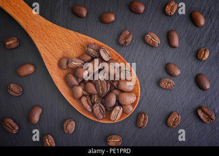 Grains de café dans une cuillère en bois sur fond d'ardoise noire. Close up. Banque D'Images