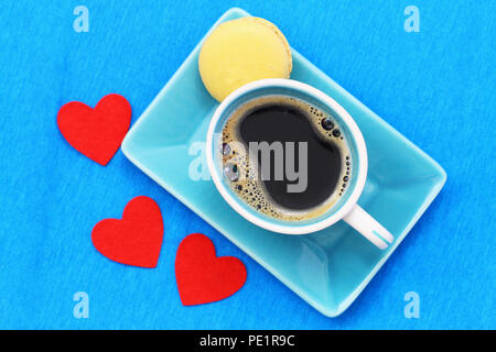 Tasse à café noir, citron et trois macarons coeurs rouges sur la surface bleue Banque D'Images