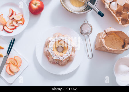 Apple pie traditionnel décoré avec du sucre en poudre entouré par des ingrédients et ustensiles de table blanc, vue du dessus. Boulangerie maison télévision jeter la nourriture com Banque D'Images