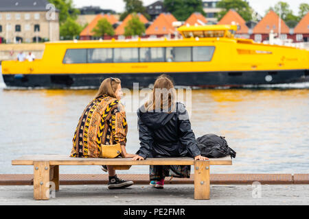 Deux jeunes femmes parlant sur banc Ofelia Square (Ofelia Plads) par le front de Copenhague, en passant par le bus de l'eau jaune Banque D'Images