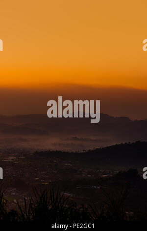 Vue sur le village entouré de montagnes et d'arbres en couches de brouillard le matin avec orange sky Banque D'Images