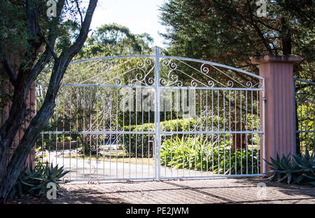 Metal blanche en fer forgé, portes d'entrée l'entrée en jeu de brique ciment pilier avec jardin résidentiel en arrière-plan Banque D'Images