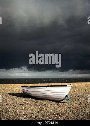 Un seul bateau en bois blanc sur une plage de galets sous un ciel d'orage. Banque D'Images